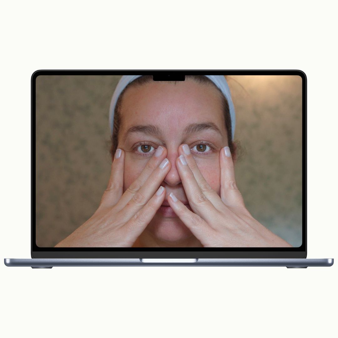 Woman demonstrating a face yoga massage technique in an online video lesson
