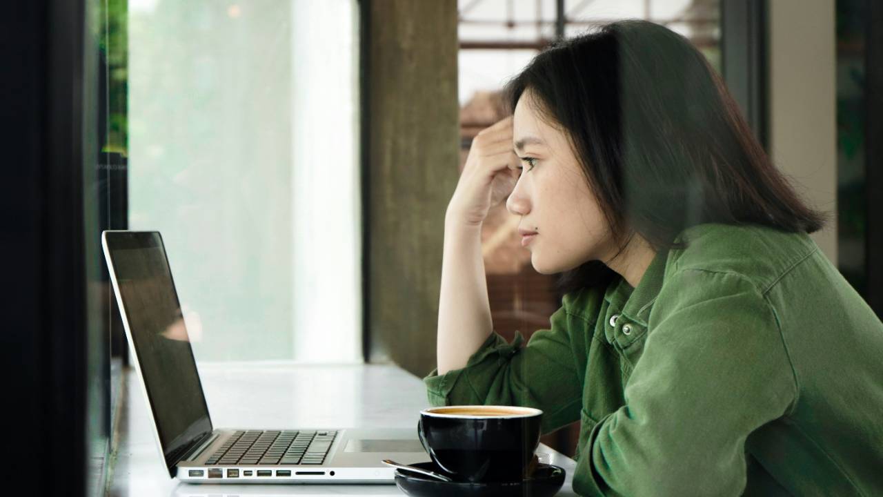 Woman sitting at a laptop with her hand pressed to her forehead, braced and holding tension while she works