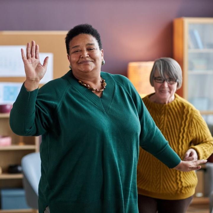 Older black women waving with her older Asian friend behind her