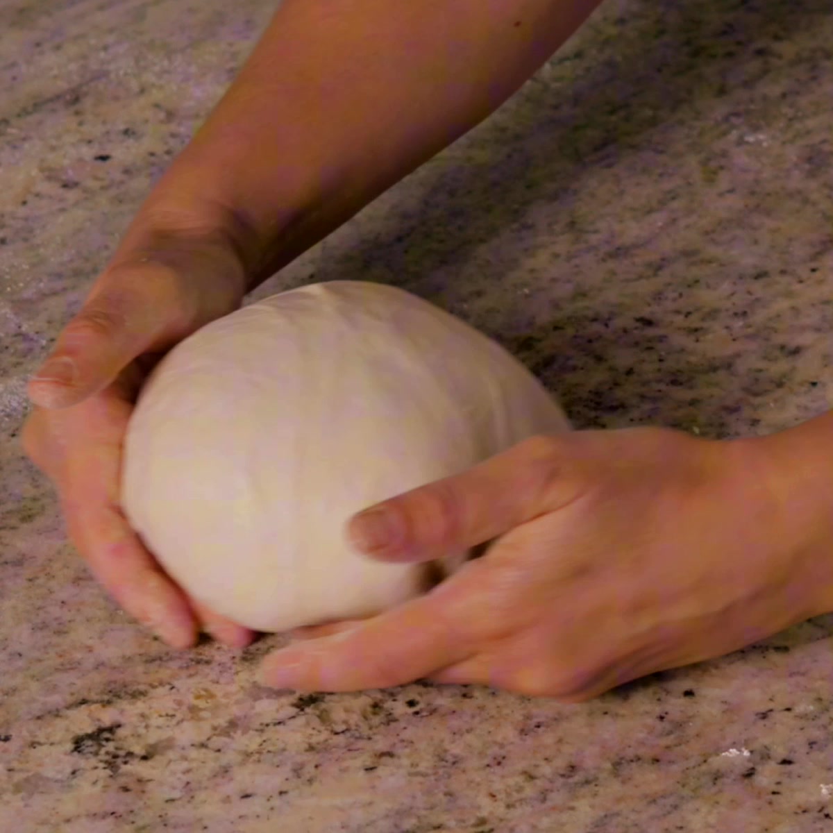 Hands shaping smooth sourdough dough