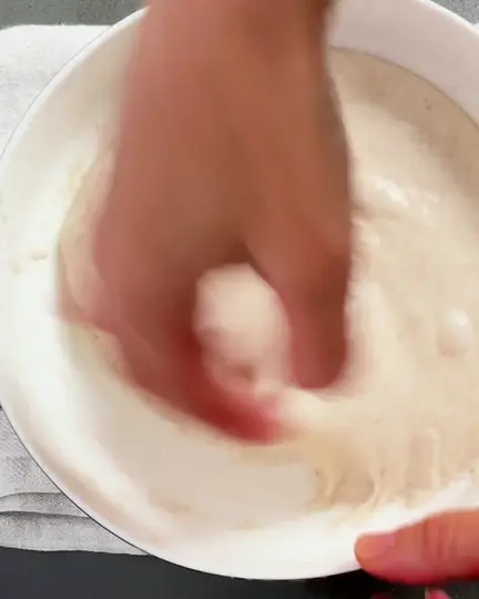 Coil folds on smooth sourdough dough in a white bowl