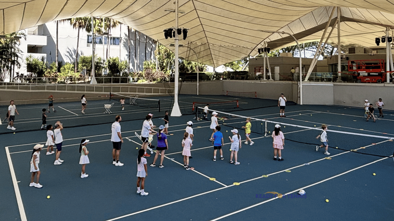 Junior tennis players taking part in a Ready for Tennis group coaching session on blue courts under shade on the Gold Coast.