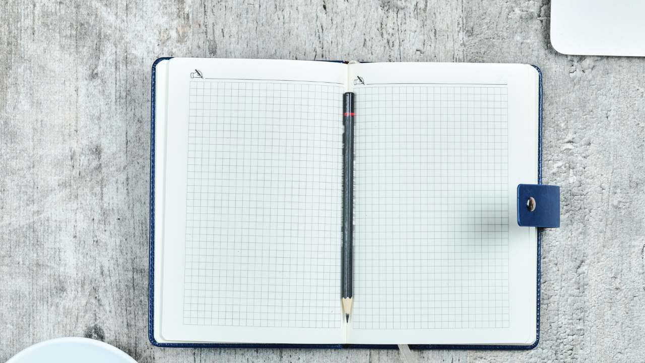 An open paper notebook on a desk showing heavily erased text that has left permanent indentations on the page, representing an inherited cultural ledger.