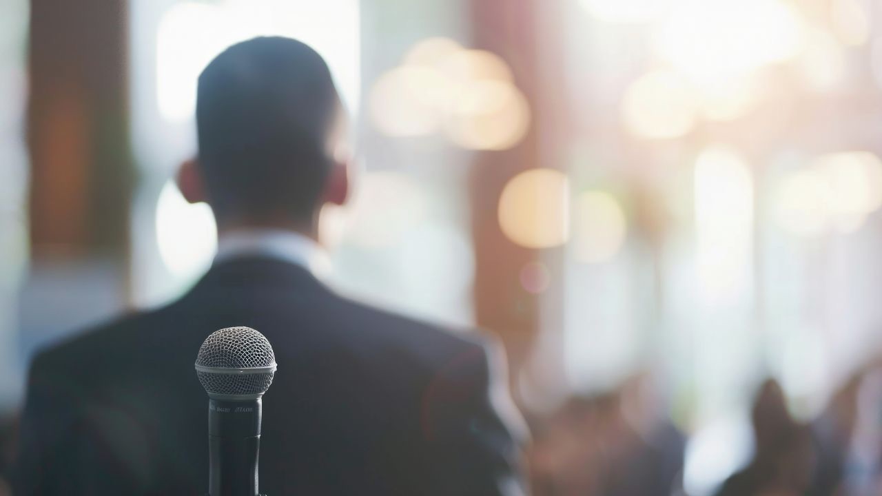 A speaker's-eye view of an audience with a note in the foreground that says 'Look closer', representing the need to see past the label of a nervous speaker