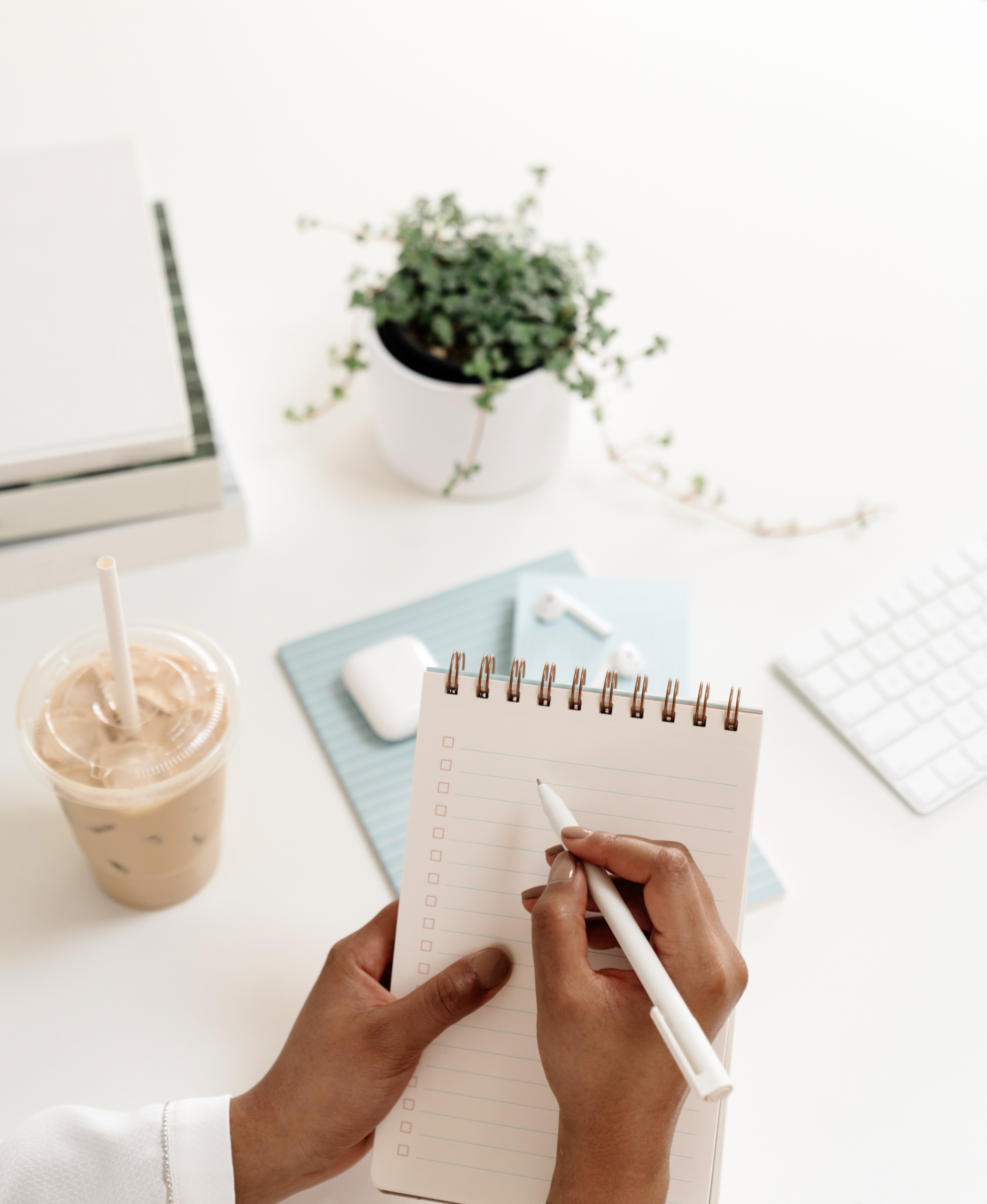 Hands writing a checklist on pale blue notepads beside a keyboard