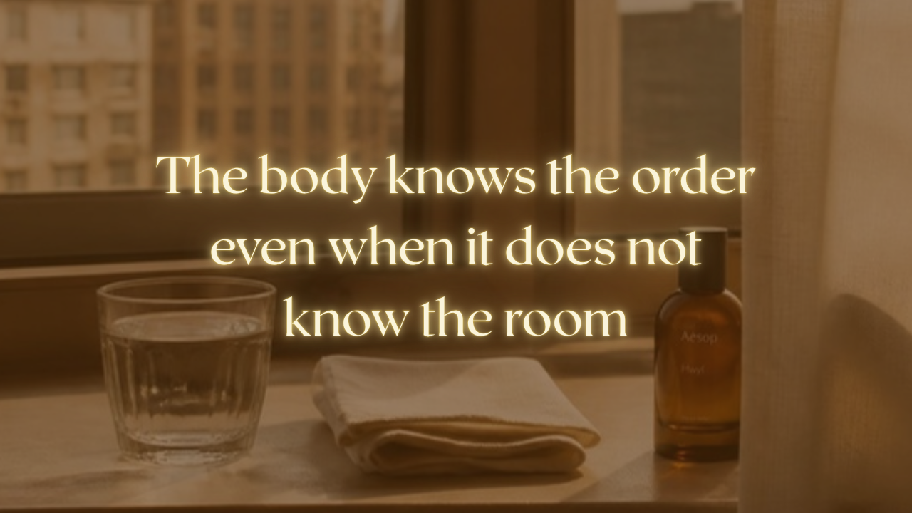 A glass of water, a folded cloth and a small amber bottle on a windowsill in low morning light