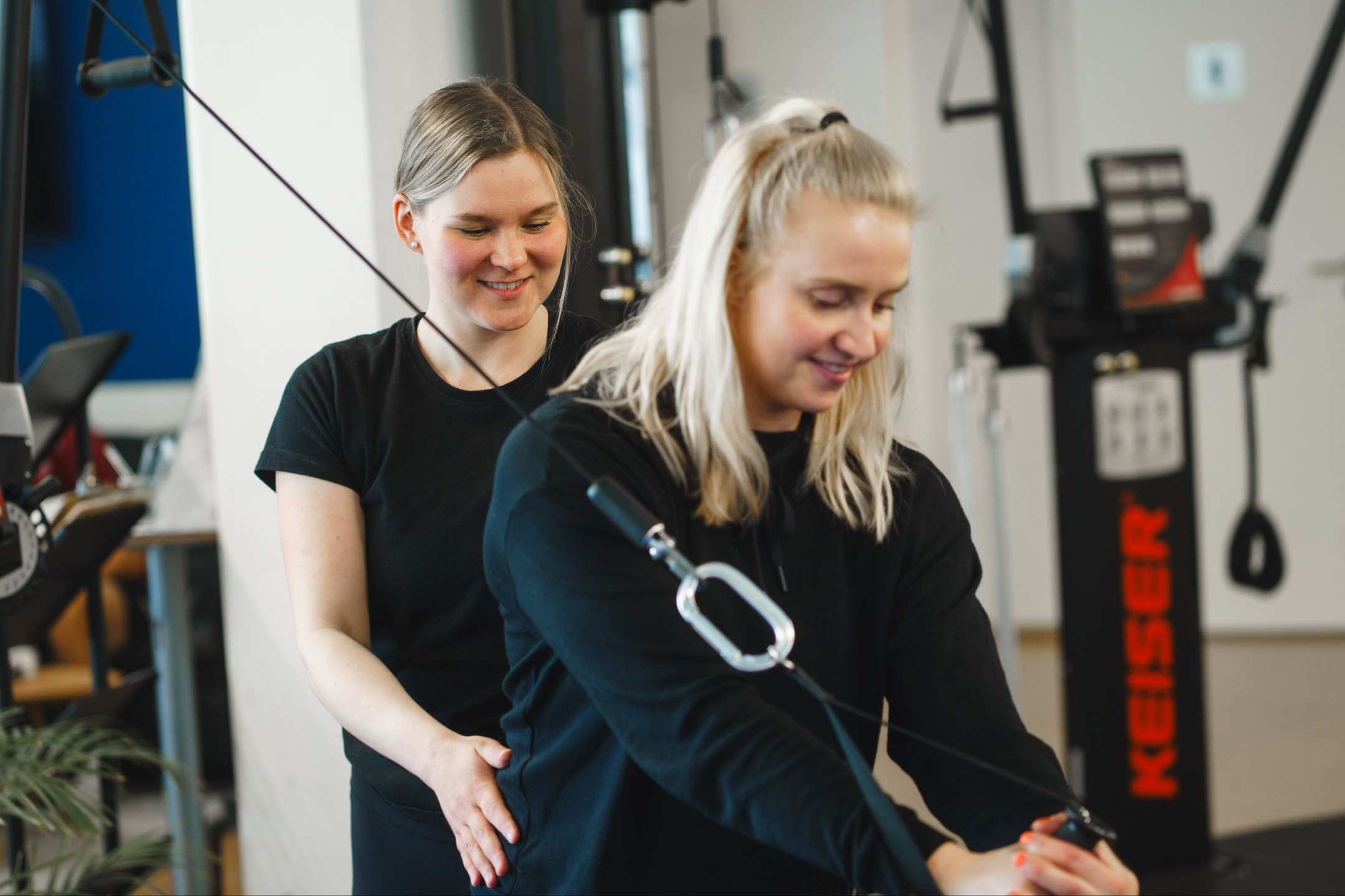 Fysioterapeutti ohjaa asiakkaalle harjoitetta kuntosaliympäristössä