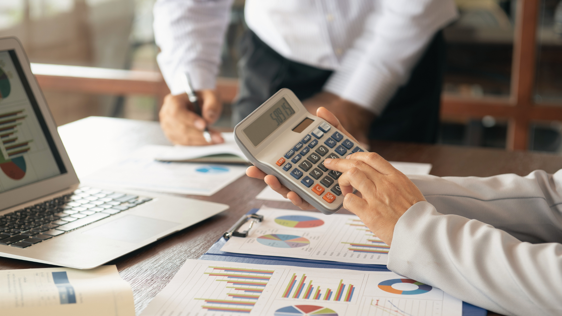 Professional reviewing charts on an iPad at a desk with a laptop and documents