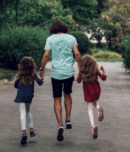 Parent and two kids running or skipping away from the camera down a road with trees in the background