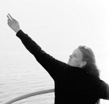  Woman standing on boat reaching up and to the side, water in the background