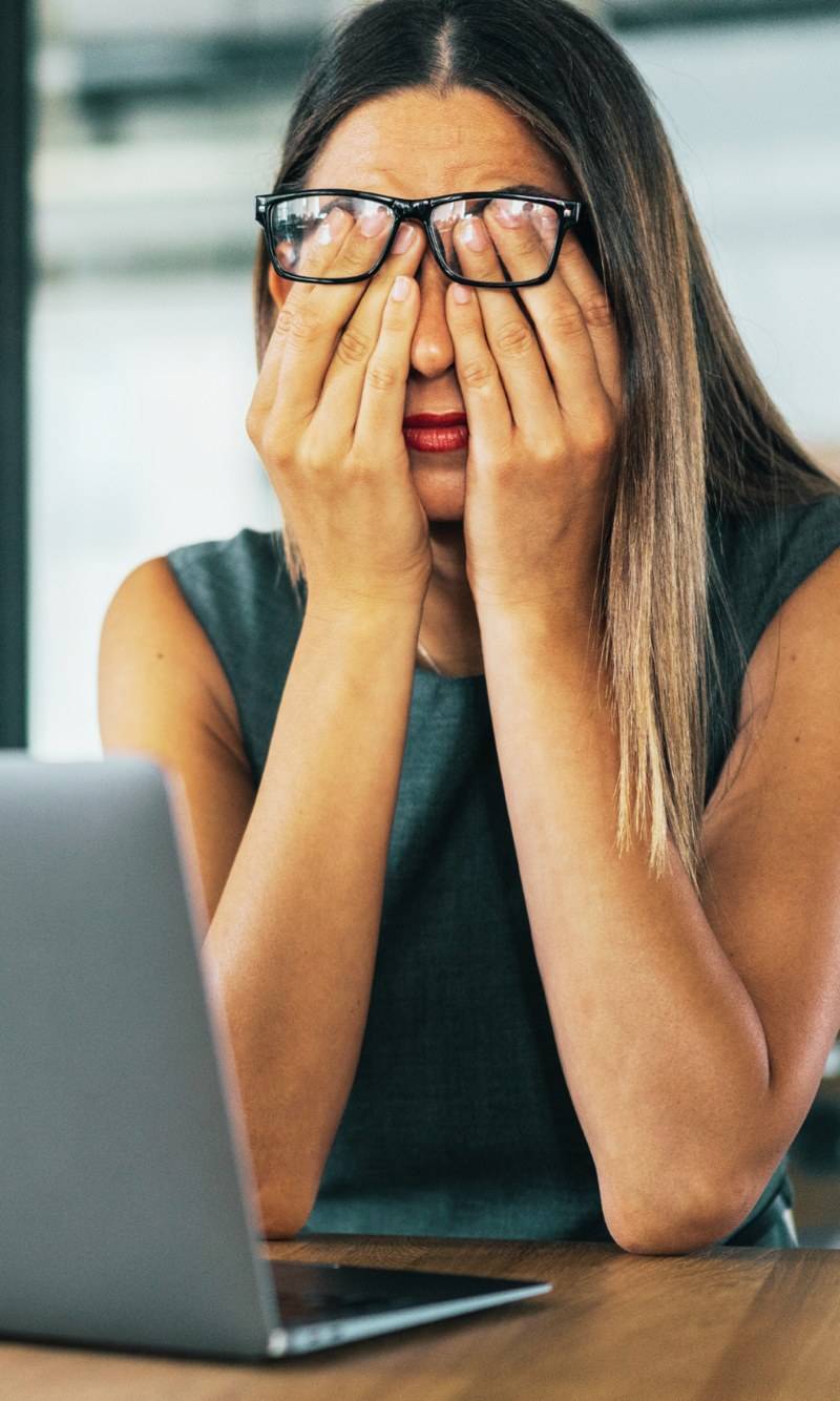 Exhausted teacher covering her face with her hands at a laptop