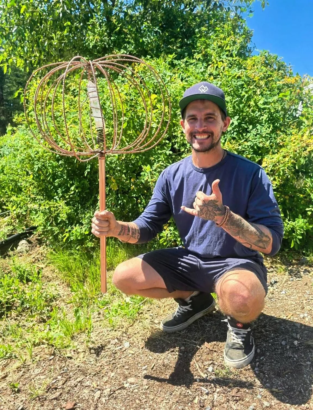 Spence Madden, founder of Frequency Gardening, crouched in the garden holding a hand-forged Harmonizer Antenna System