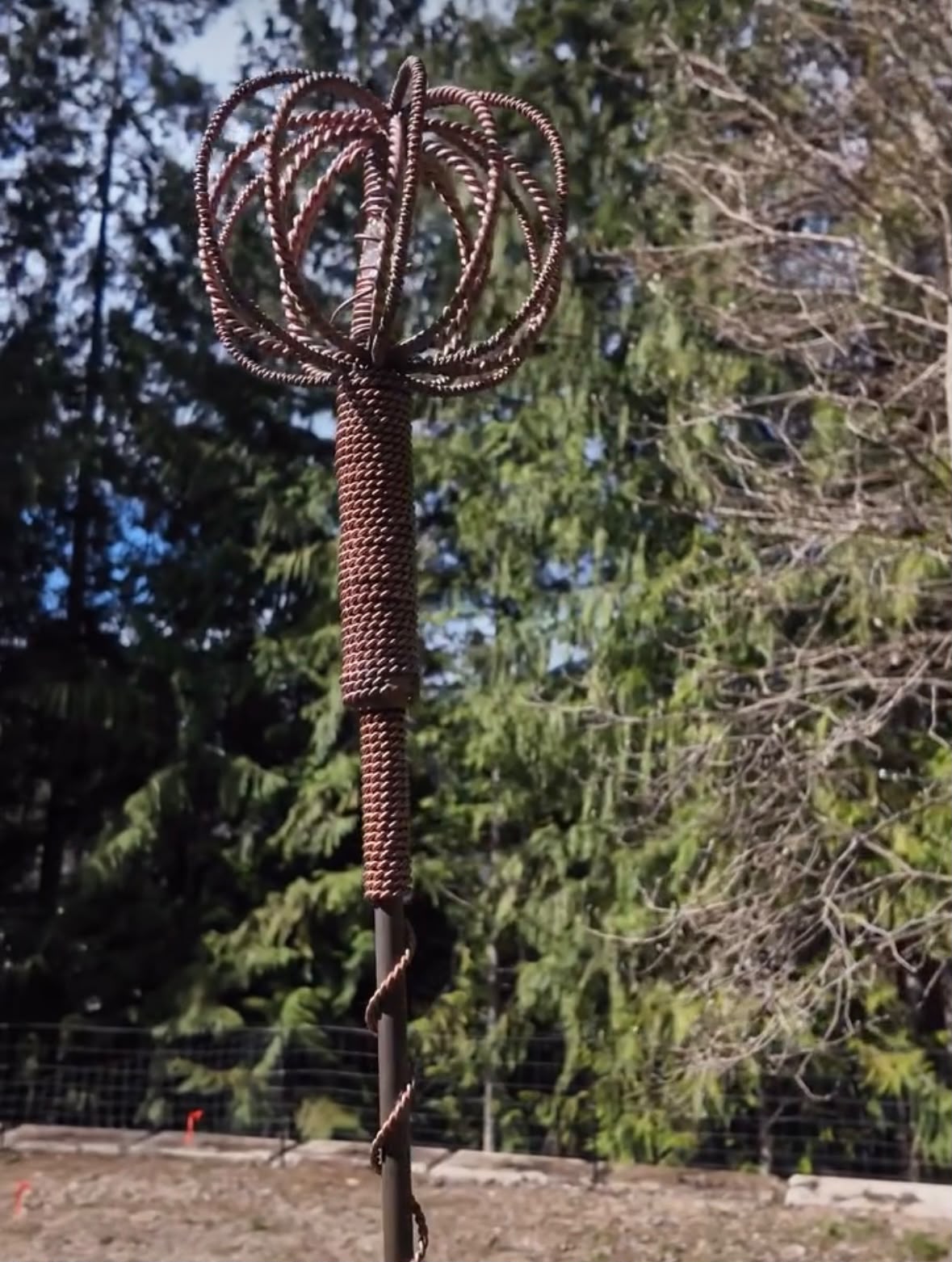 A Homestead Harmonizer Antenna System standing in a fenced field beside the forest