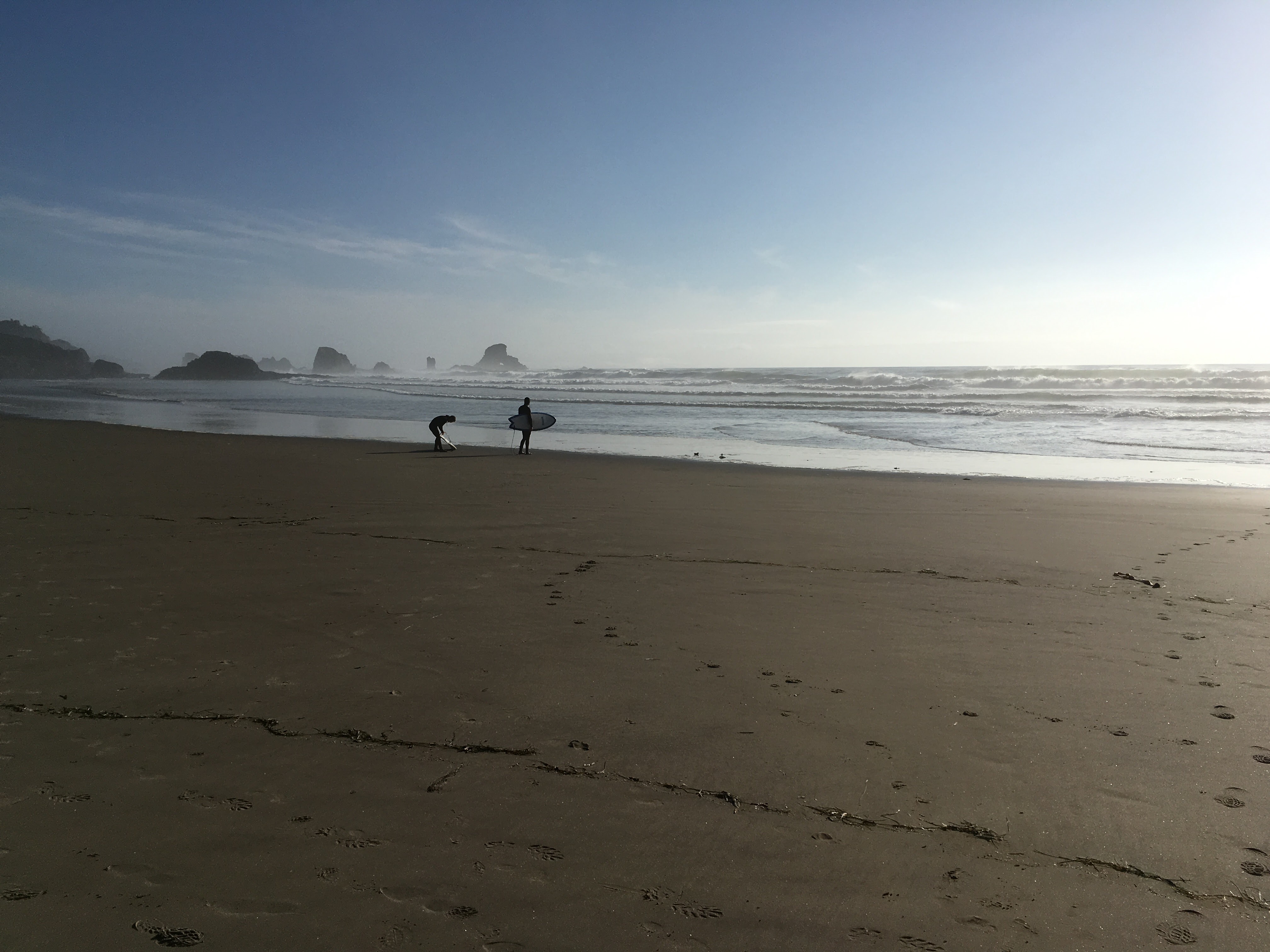 Two surfers on a beach along the Oregon Coast with big rocks in the background