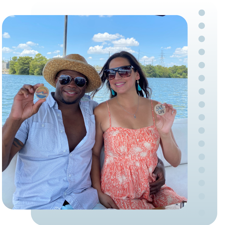 A man and woman smiling on a boat, holding up round iLN Adventure Tokens
