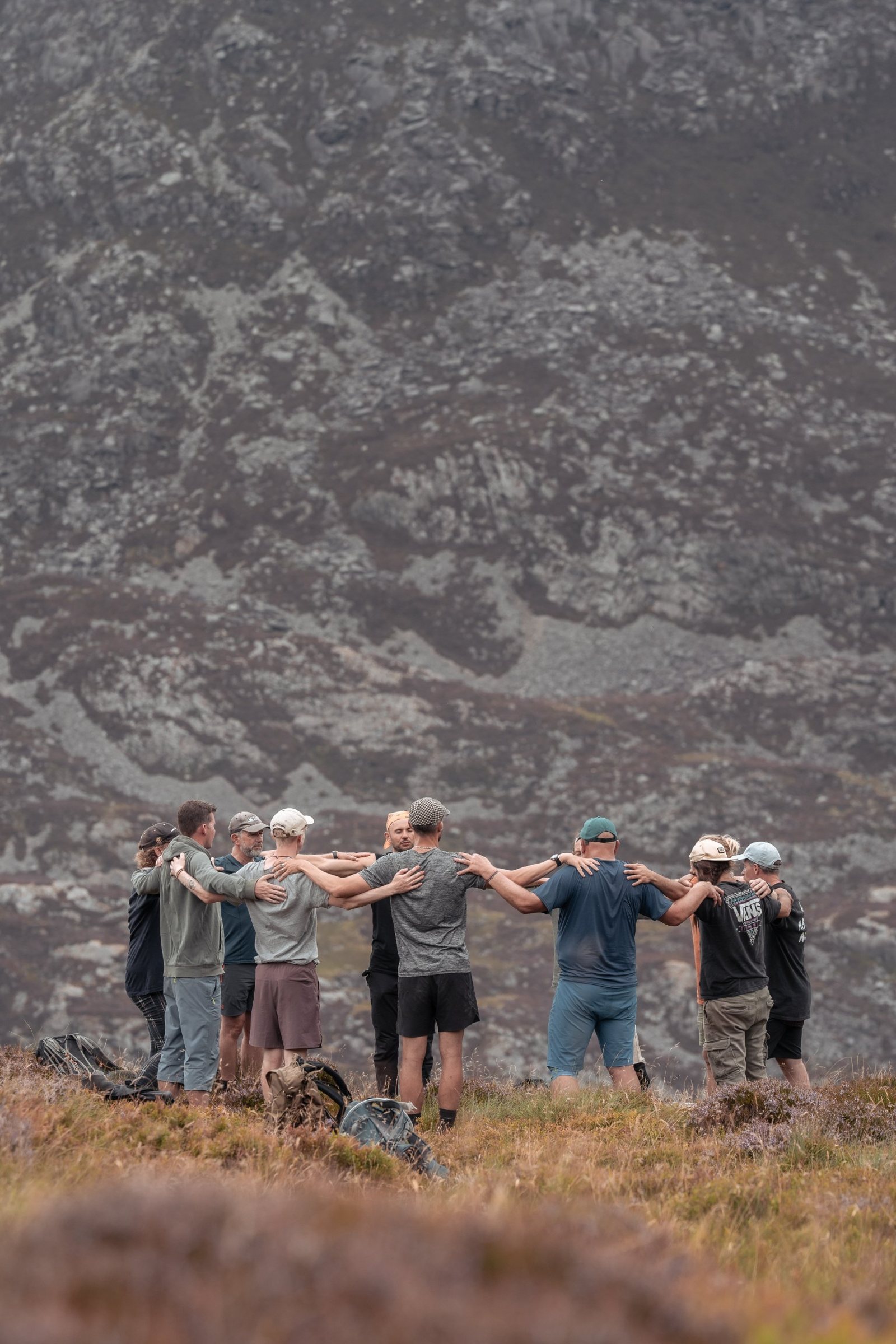 Men standing in a circle with arms around each other on a hillside