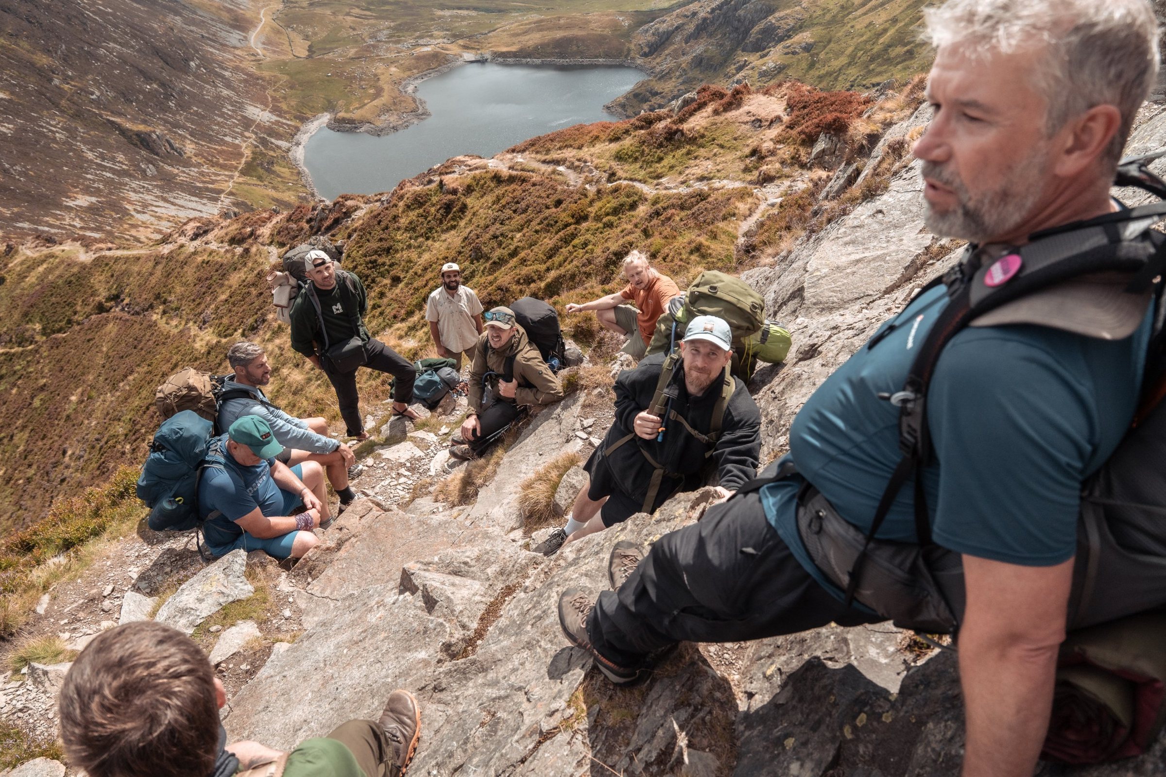 Men resting on a rocky ridge above a mountain lake