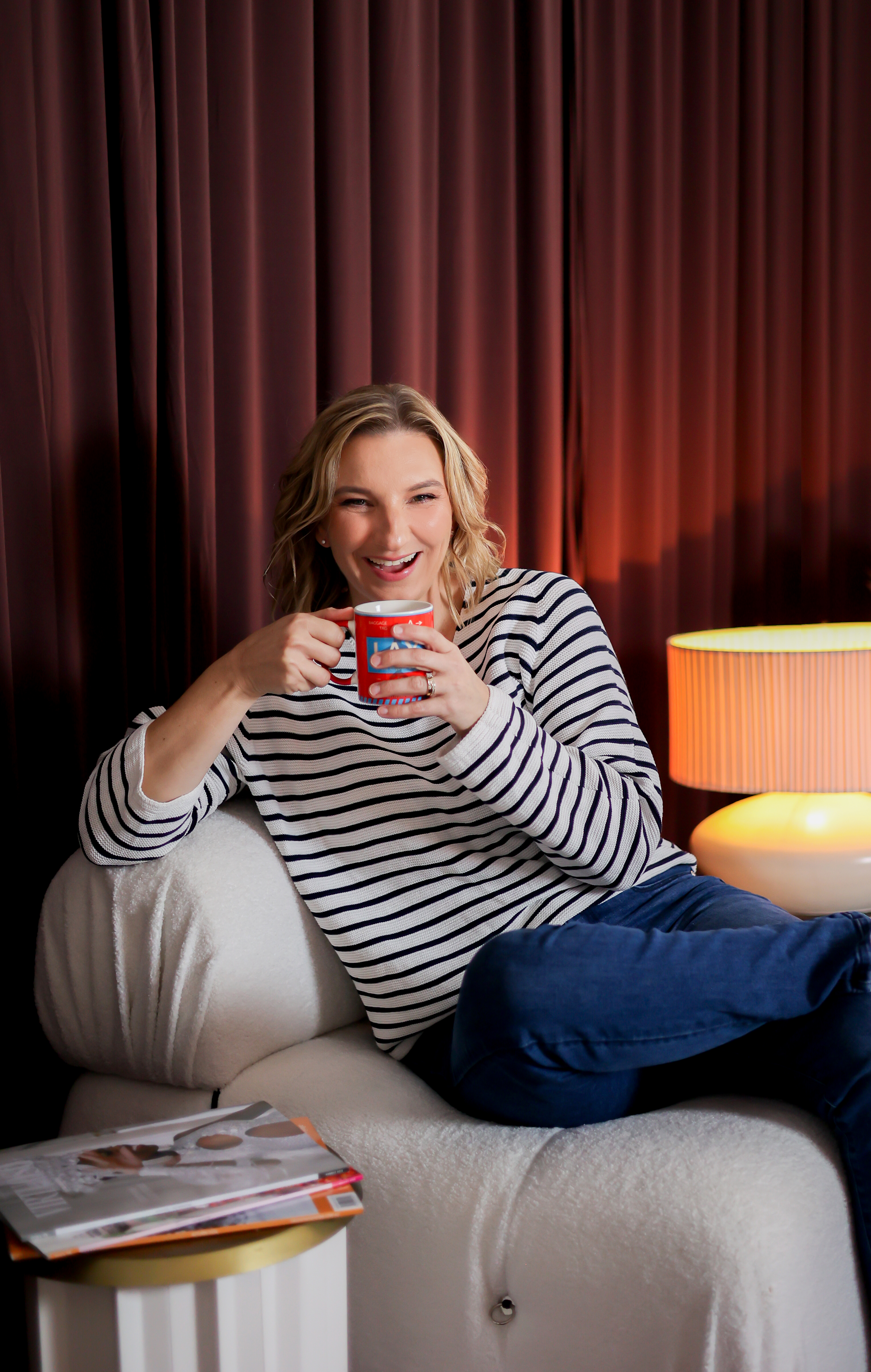 Roslyn Ranse laughing on a couch with a cup of tea