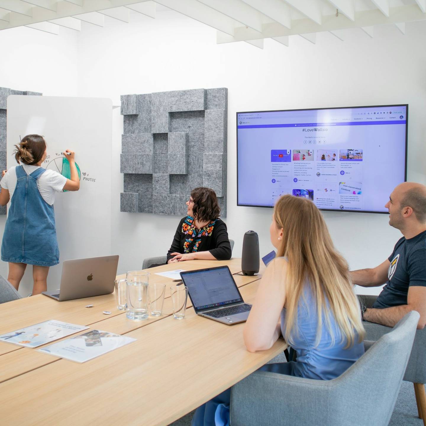Lady drawing a chart on white board with two women and one man watching in a lecture room