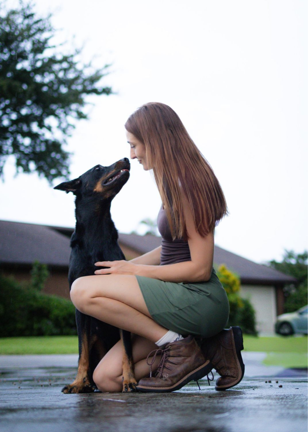 Savanah kneeling face to face with her Doberman, sharing a playful moment outdoors