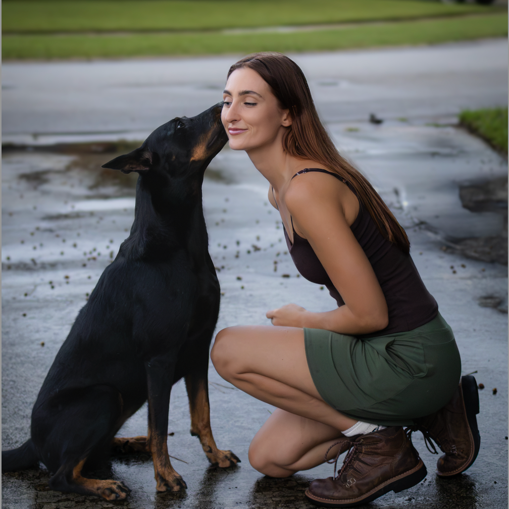 Savanah kneeling outdoors as her Doberman gives her a kiss