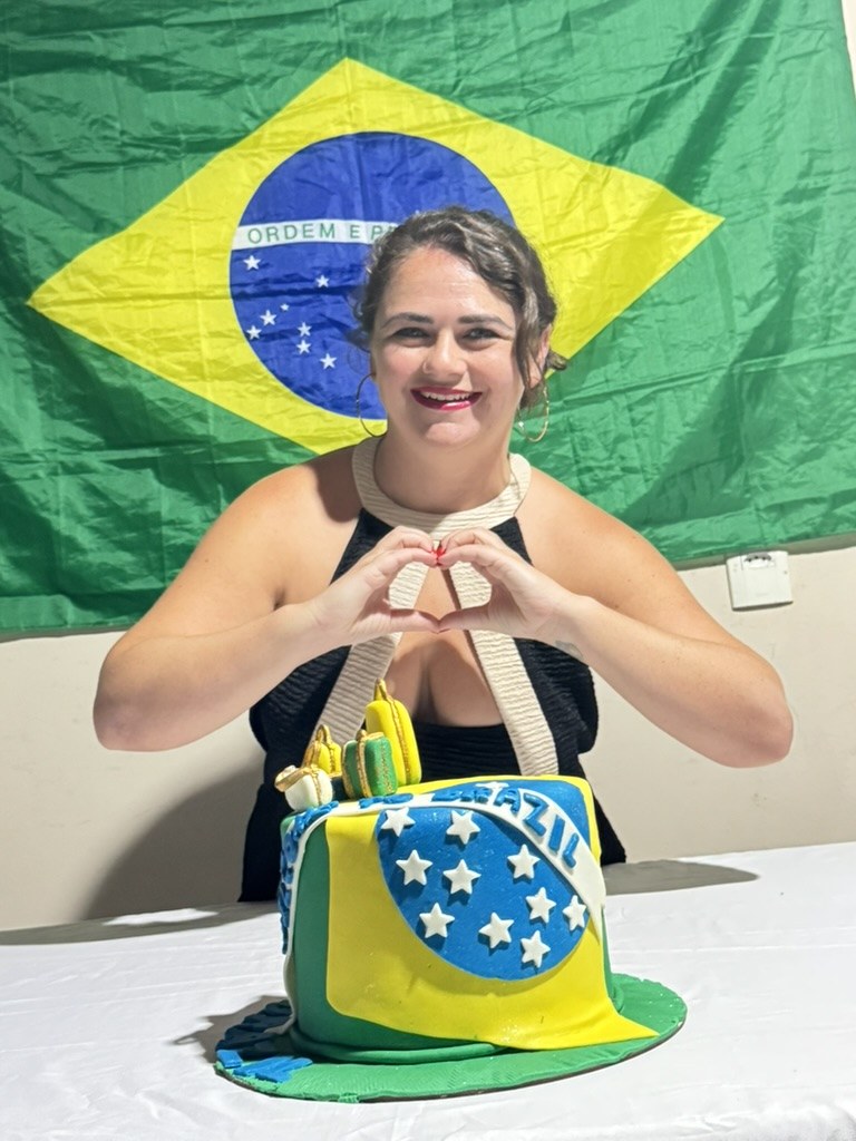 River making a heart with her hands in front of a Brazilian flag and a Brazil-themed cake