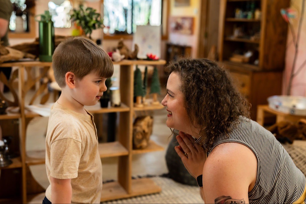 A teacher kneeling to talk with a young boy in the classroom