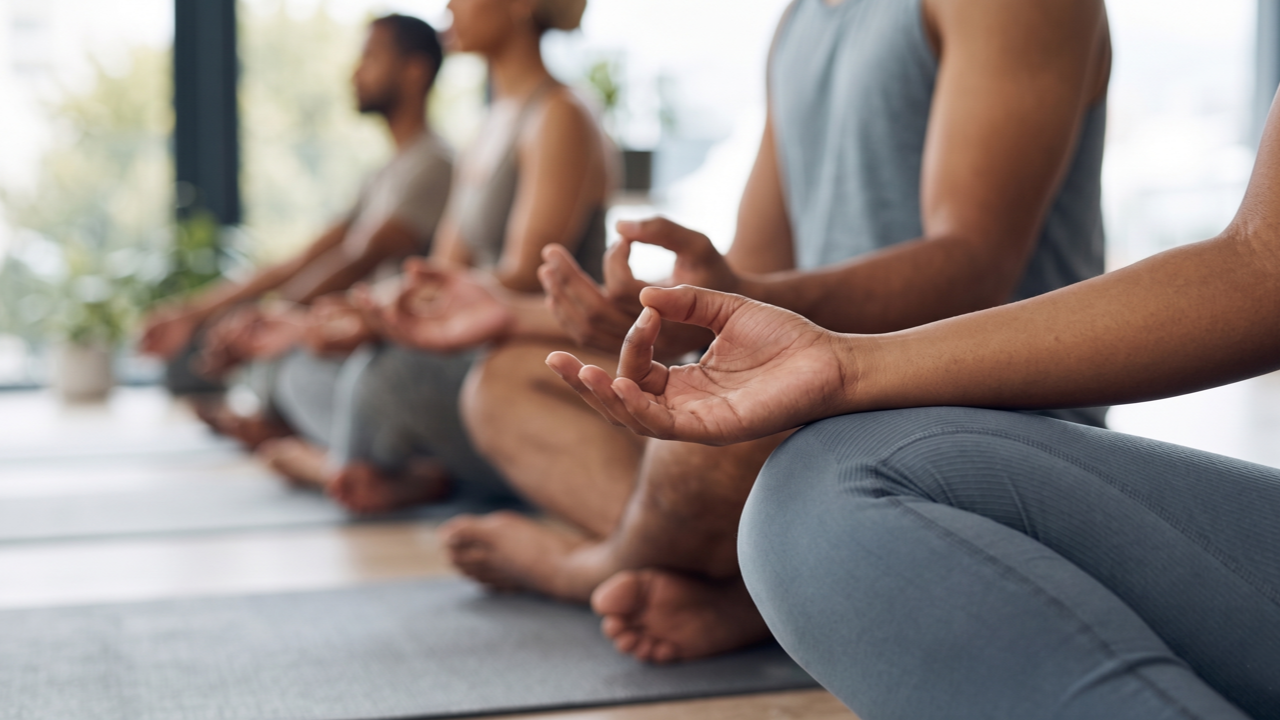 A detailed close-up shot of students' hands in Gyan Mudra (thumb and index finger touching) while resting on their knees during a seated meditation.
