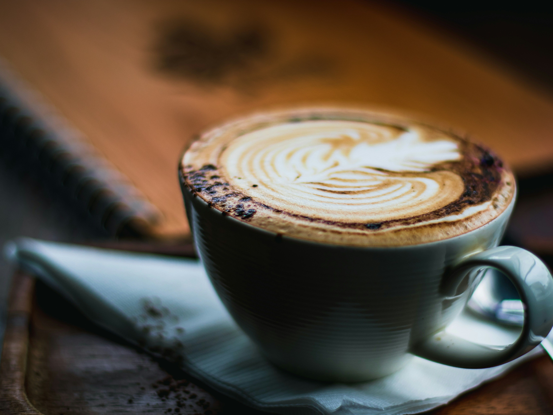 Coffee in a rustic blue cafe cup with chocolate dusting and warm wood table underneath