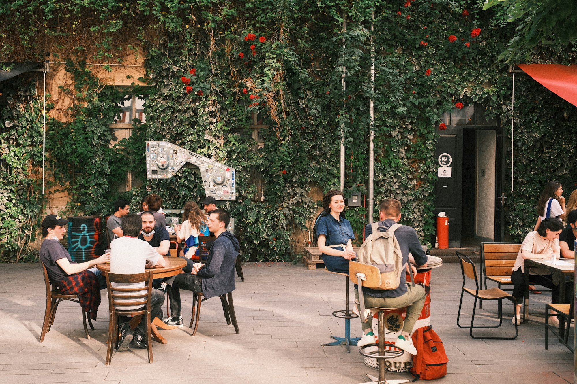 Friends talking at tables in a vine-covered courtyard