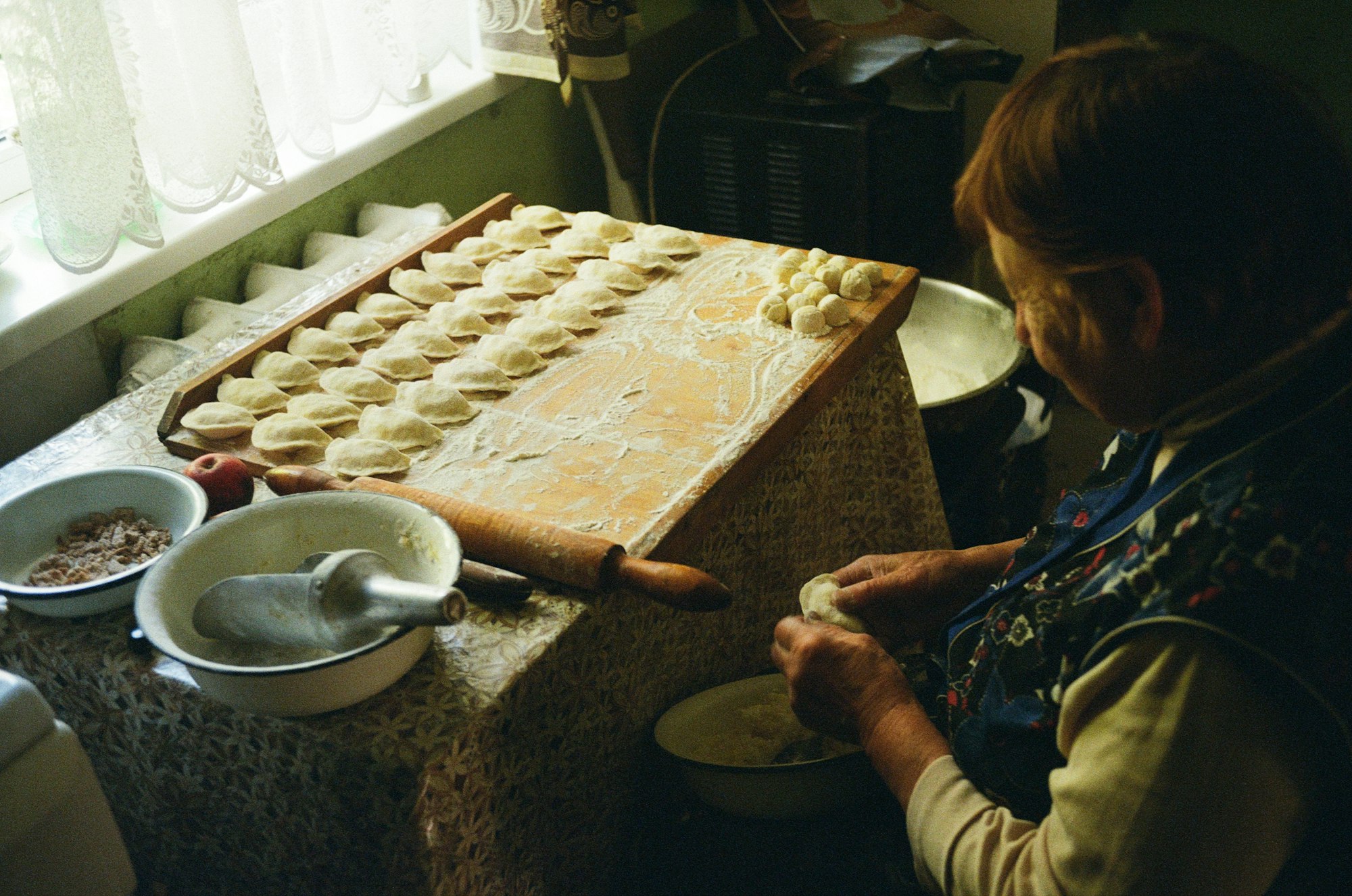 Older woman makes dumpling dough at a kitchen table by a window