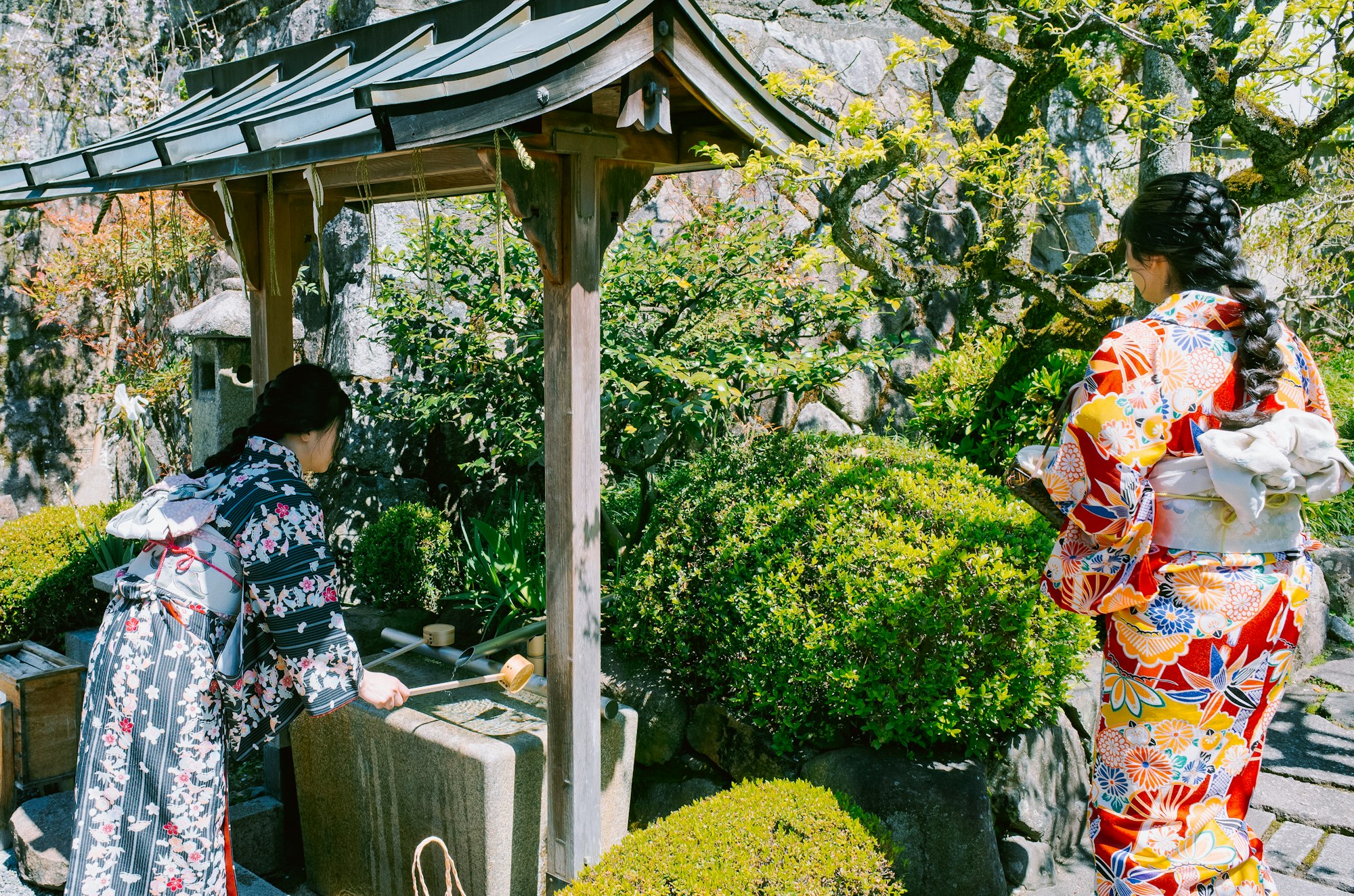 Two women in kimono at a shrine water basin performing a hand-washing ritual