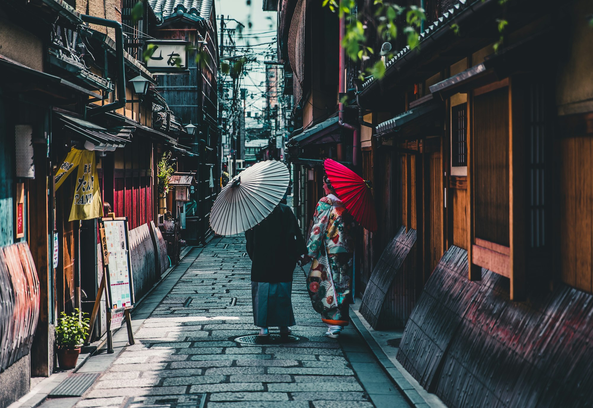 Two women walking away down a stone lane in Kyoto, one under an umbrella