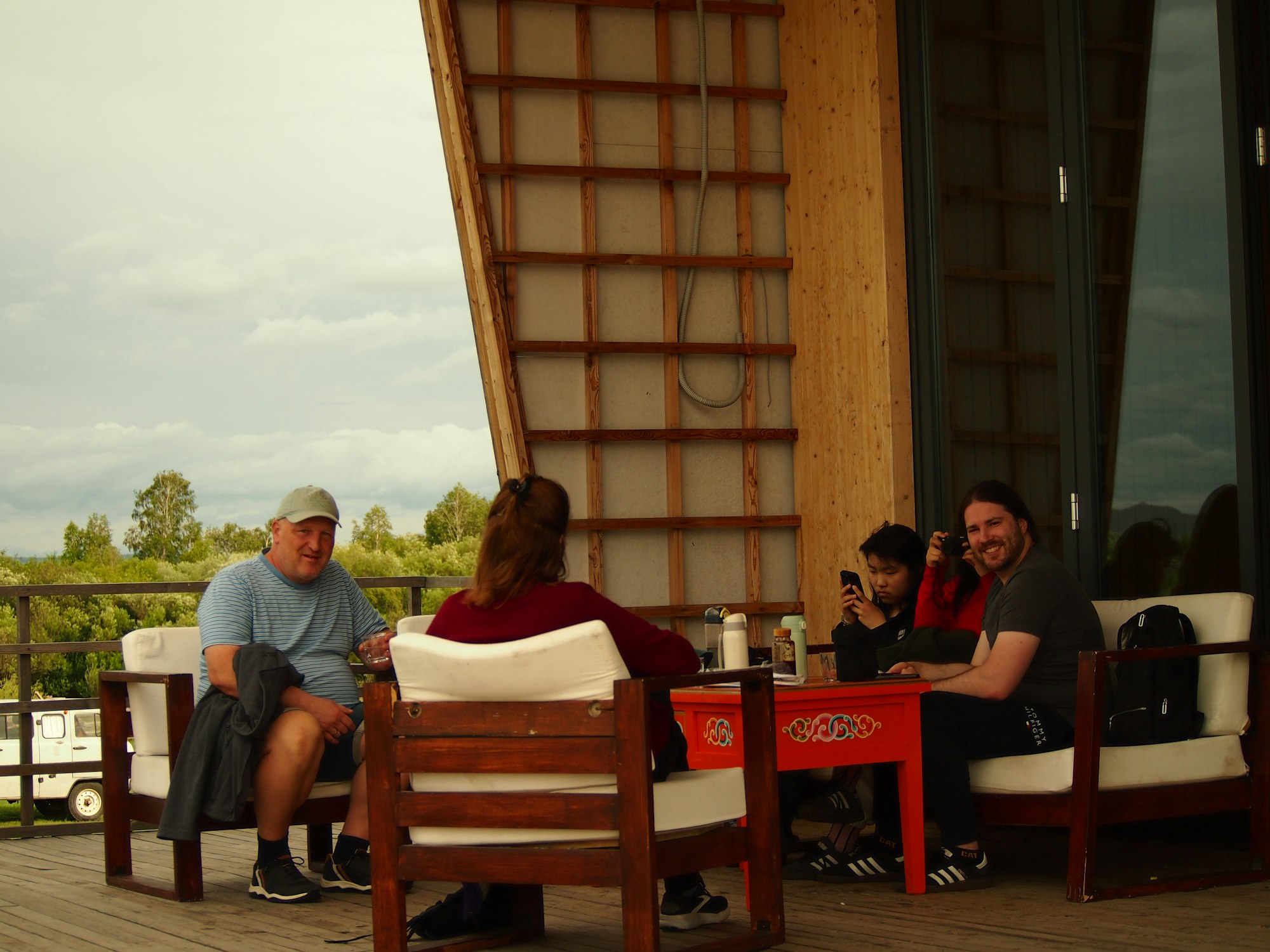 Four people talk casually on a patio under a cloudy sky