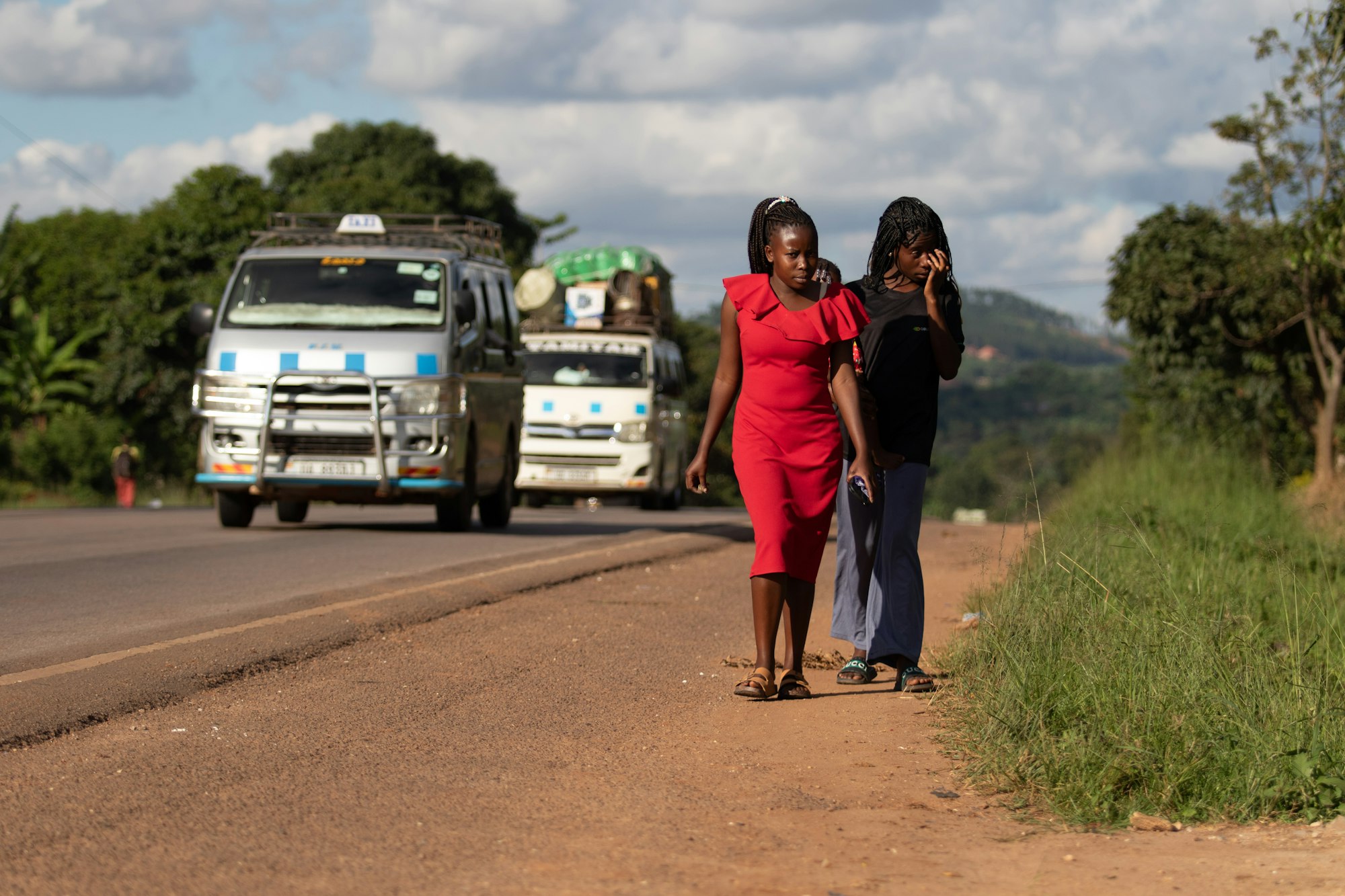 Two women walking along a roadside as a minibus passes