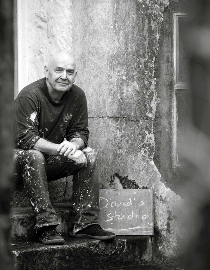 Portrait of contemporary abstract landscape artist David Mankin outside his Cornwall art studio, wearing paint-splattered clothes and smiling at the camera.