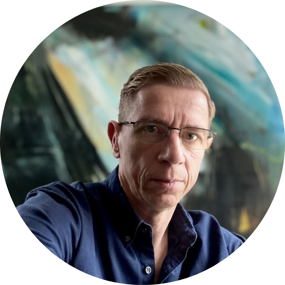 Portrait of a male artist wearing glasses, seated in front of a large abstract painting in a studio setting.