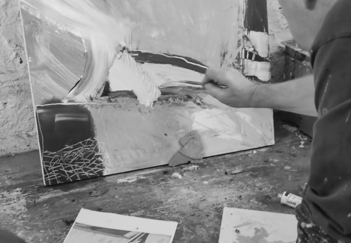 Close-up of artist David Mankin using a palette knife to apply paint to an abstract landscape artwork on a canvas in his studio.