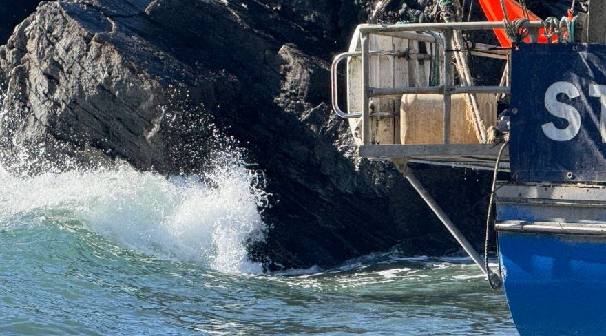 Waves crashing against the rocky Cornwall coastline beside a fishing boat, capturing the coastal inspiration behind David Mankin's contemporary abstract landscape paintings.