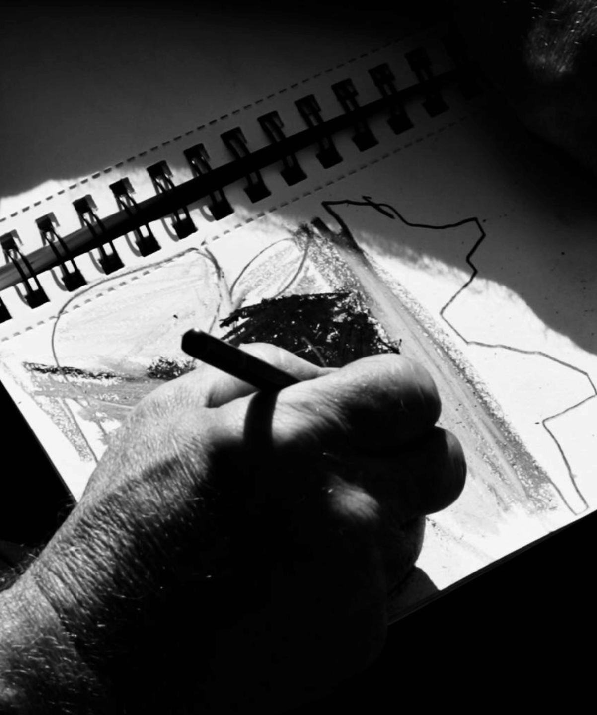 Black and white close-up of an artist’s hand sketching expressive landscape lines in a notebook, capturing the early stages of an abstract composition.