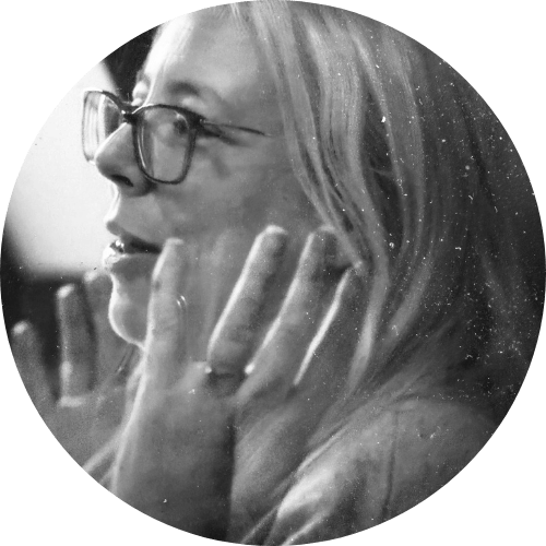 Black and white profile portrait of a woman with glasses, gently touching her face as she listens, captured in a candid moment.