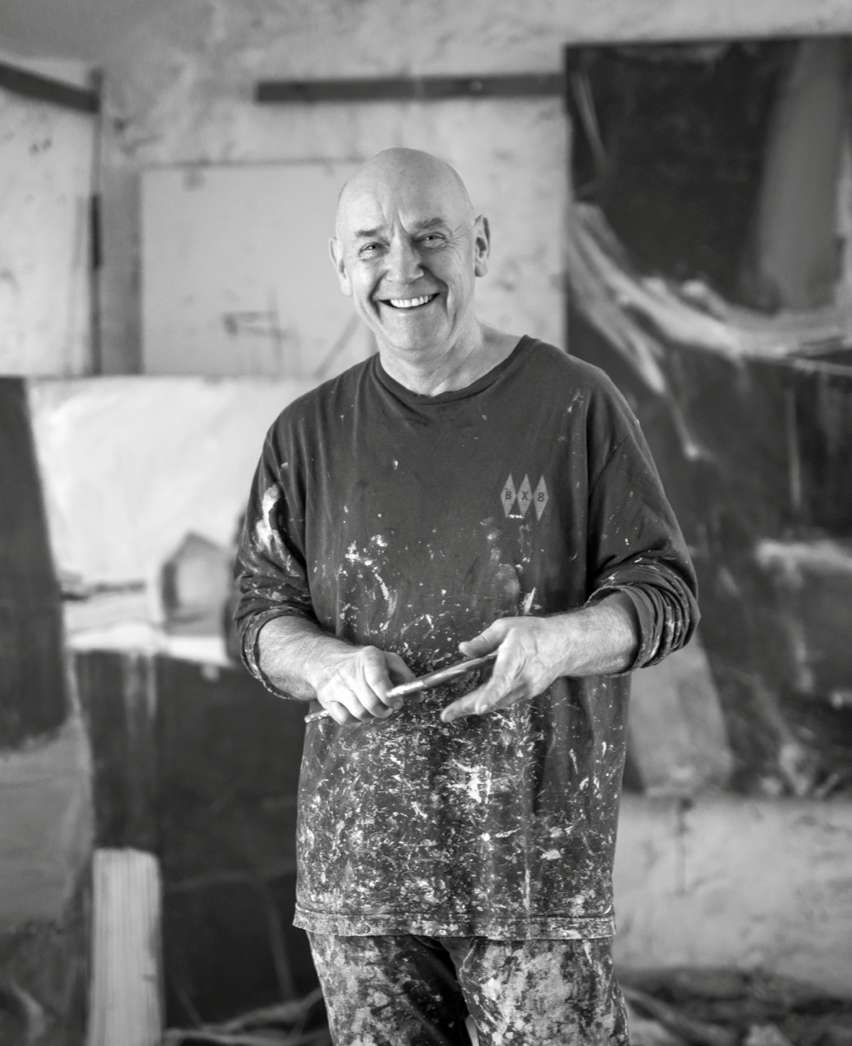 Portrait of contemporary abstract landscape artist David Mankin standing in his Cornwall art studio with paint-covered clothes and a palette knife.