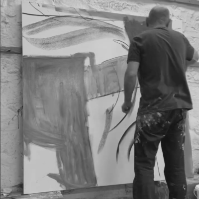 Black and white photo of David painting energetically on a large canvas in his studio, using expressive brushstrokes with paint-splattered clothing.