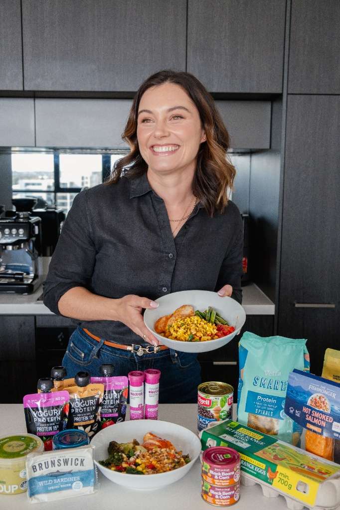Becky May, Accredited Practising Dietitian, smiling in her kitchen holding a bowl of food