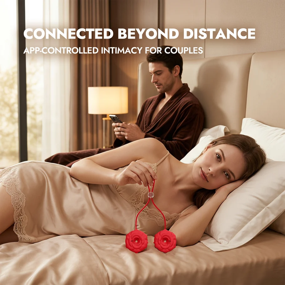 A pair of red rose-shaped app-controlled nipple toys joined by a cord, held by a woman reclining on a bed while her partner holds the phone
