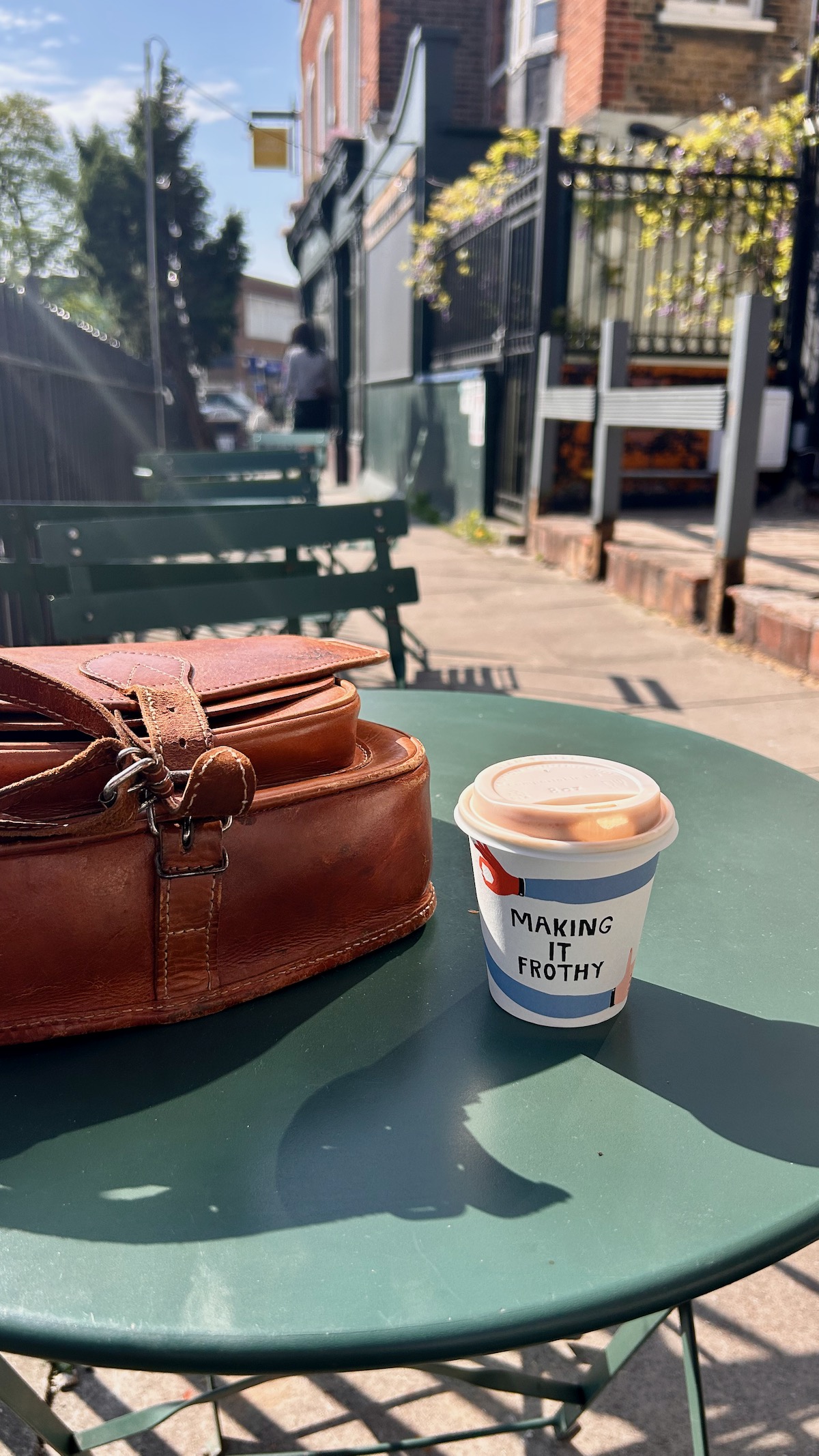 Leather bag and coffee on a green bistro table, organised creative business owner