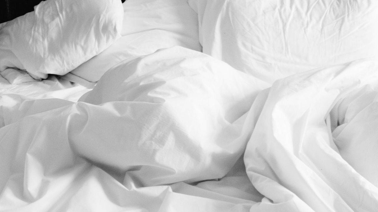 Lit défait aux draps et oreillers blancs froissés, pour illustrer le lien entre changement d’heure et sommeil