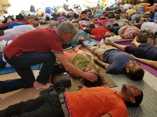 Roberto Suárez kneeling beside people lying on mats, guiding a group breathwork session