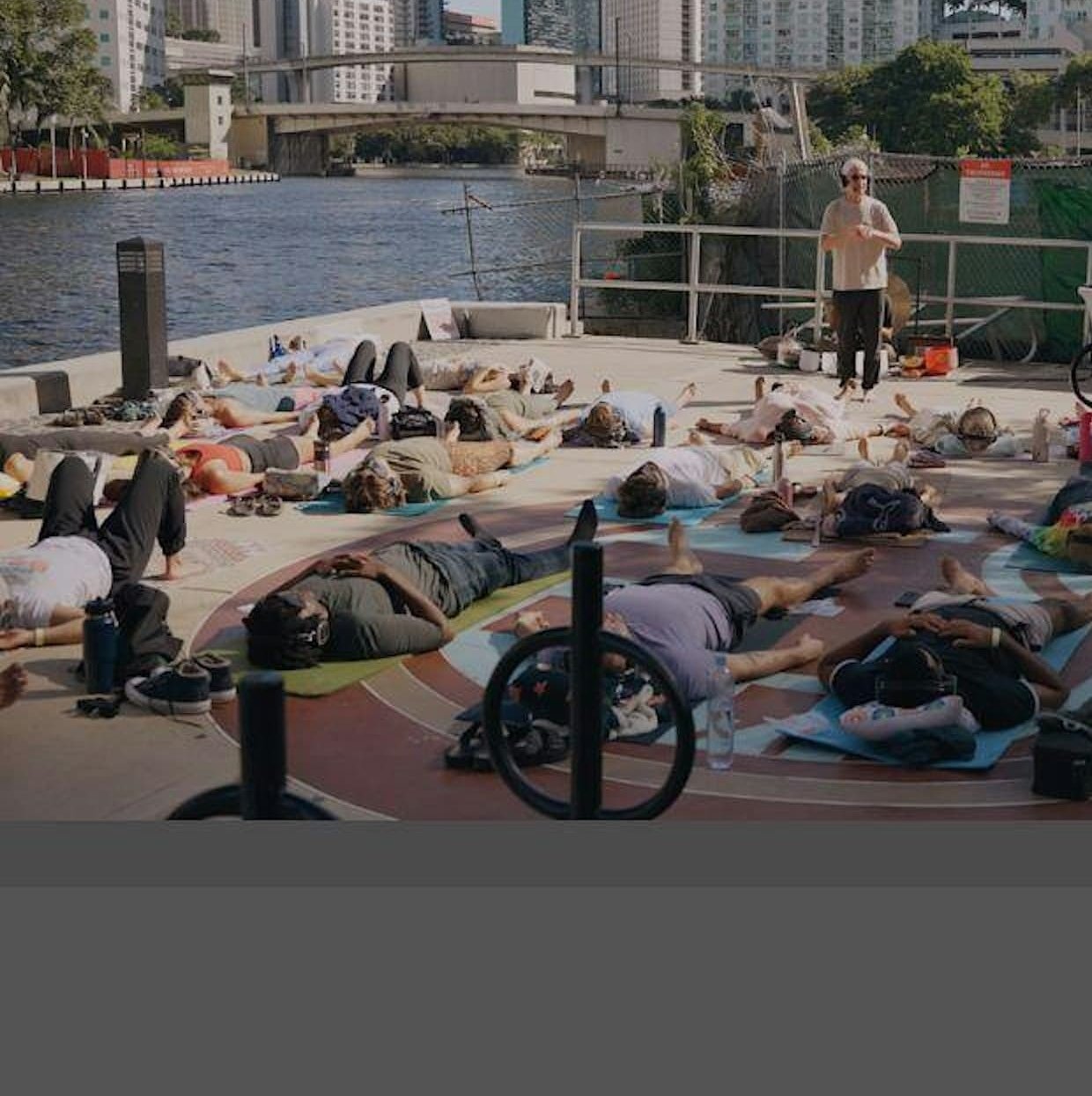 A large group lying on mats at an outdoor riverfront breathwork event in Miami