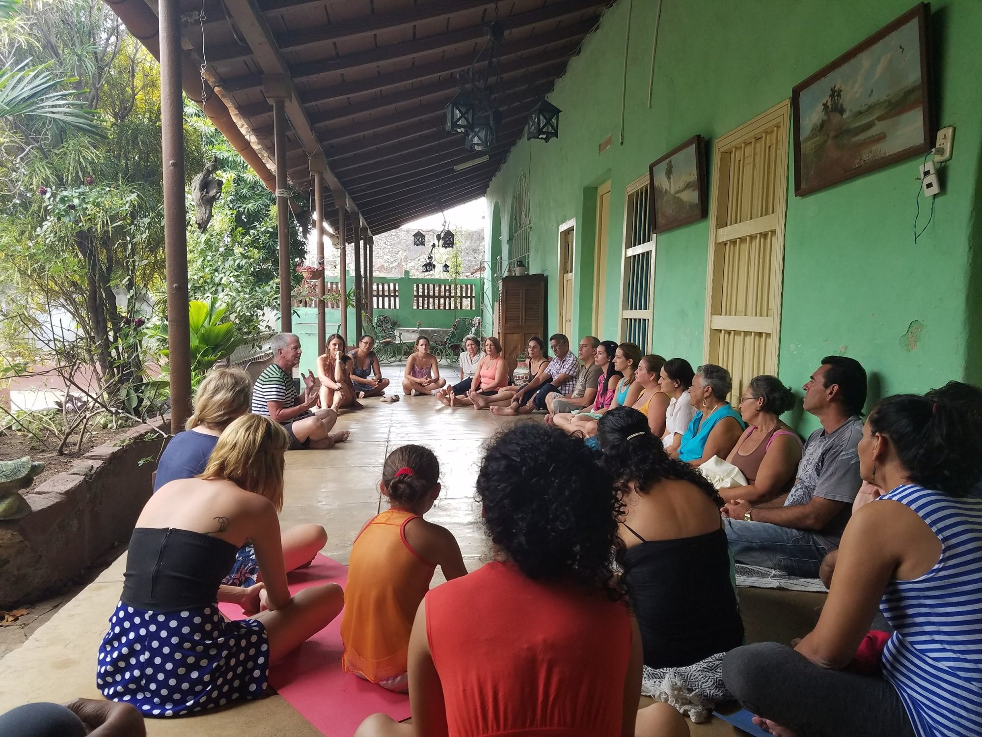 Roberto Suárez sitting in a circle with a group on a shaded veranda, talking before a breathwork session